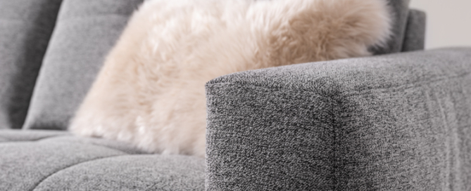 Armlehne von grauem Sofa mit flauschigem Kissen