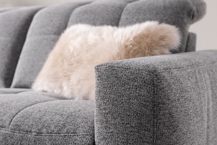 Armlehne von grauem Sofa mit flauschigem Kissen