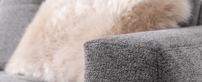 Armlehne von grauem Sofa mit flauschigem Kissen