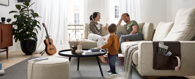 Eltern sitzen entspannt auf dem beigen Sofa, Kind spielt am Couchtisch