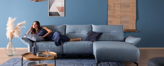 Frau liegt am blauen Ecksofa SALVIA in einem blau gestalteten Wohnzimmer