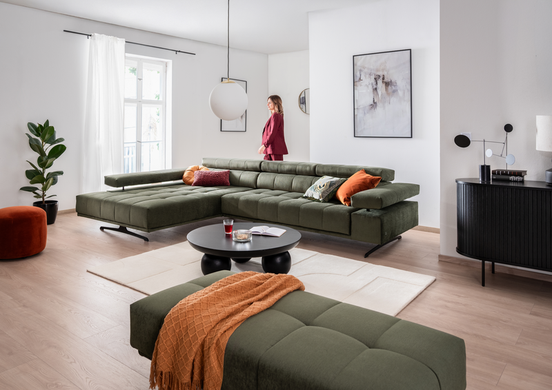 Eine Frau geht hindert dem Sofa RAIMO durch das Wohnzimmer