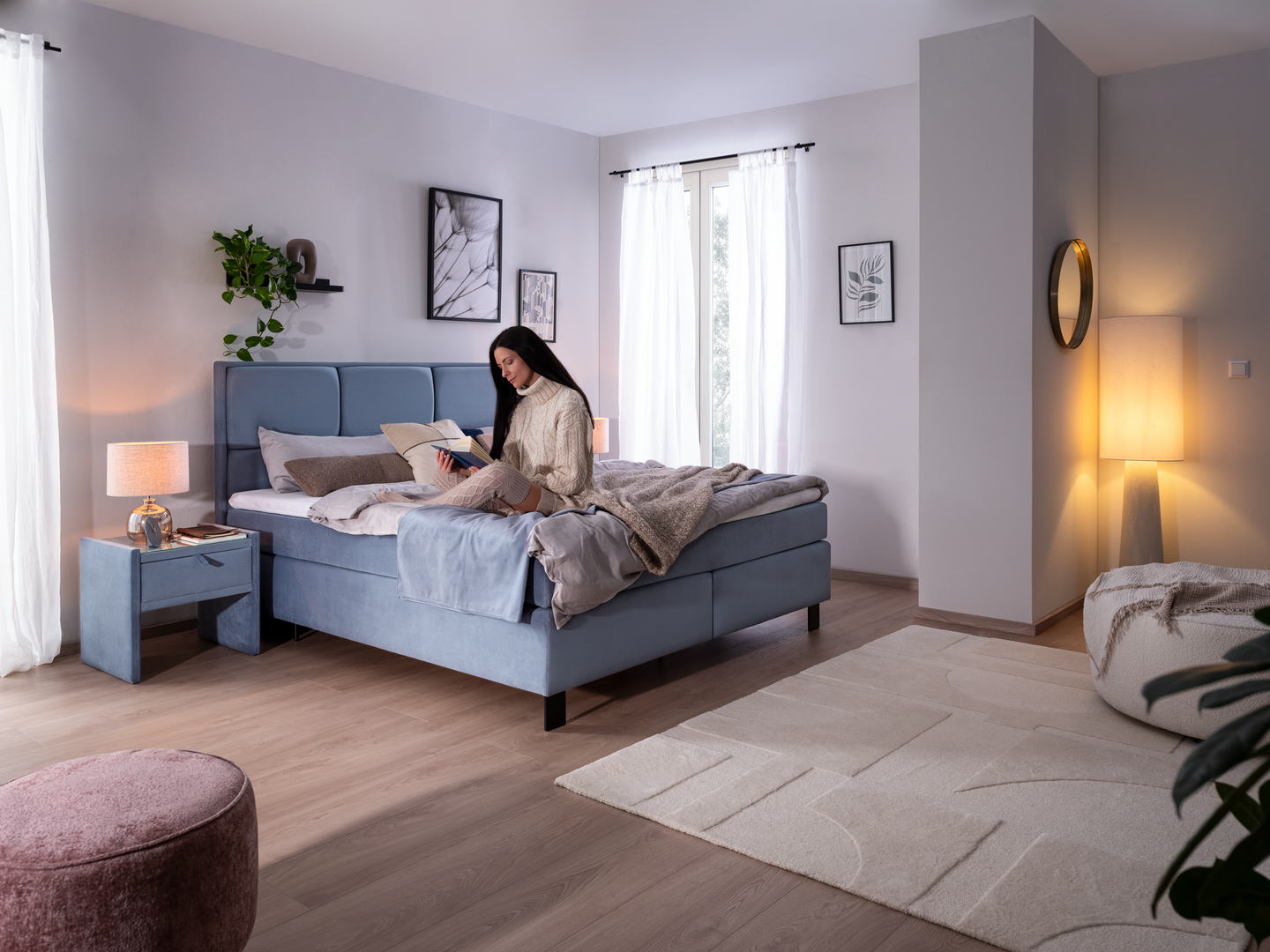 Frau sitzt auf dem hellblauen Boxspringbett Sidus und liest ein Buch