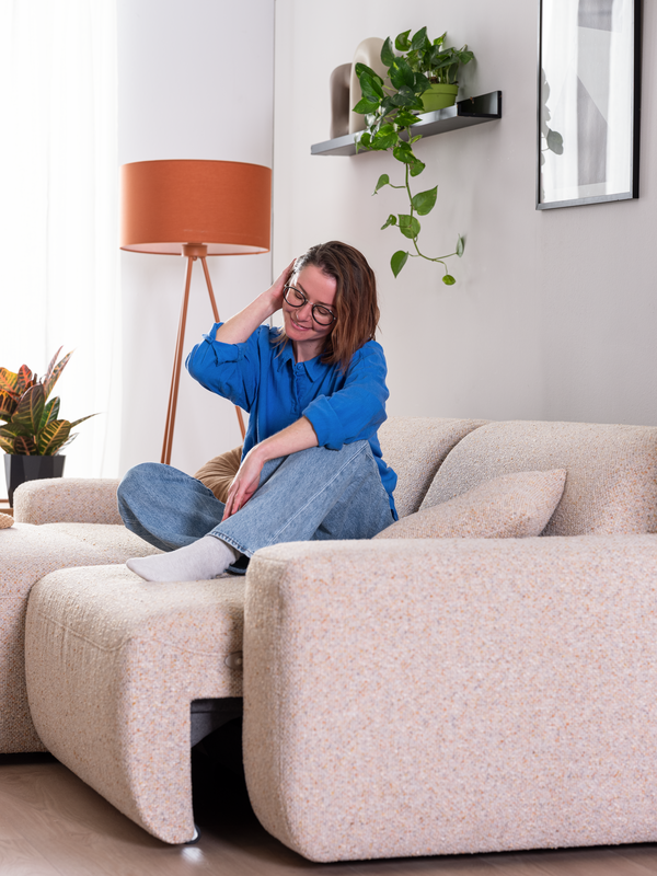 Frau sitzt auf Sofa PINEA mit Vorziehfunktion und fährt sich durchs Haar